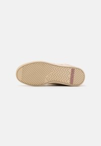 Beige színű sneaker talp texturált gumiból, cikkcakk mintázattal és lila logó akcentussal. Lapos dizájn, amely alkalmas mindennapi viseletre.