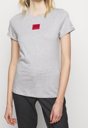 Gray cotton t-shirt featuring a red rectangular logo patch with "HUGO" text. Short sleeves and a crew neckline, casual fit.