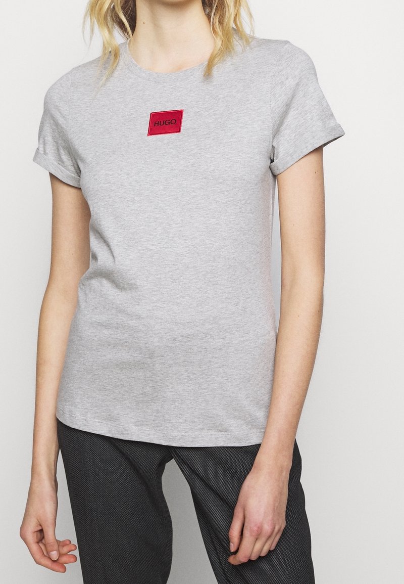 Grå bomulds T-shirt med et rødt rektangulært logo-patch med teksten "HUGO". Korte ærmer og rund halsudskæring, afslappet pasform.