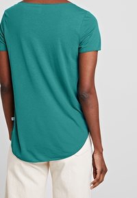 T-shirt blu-verde a maniche corte con orlo arrotondato, realizzato in tessuto morbido, presenta una vestibilità comoda e un dettaglio di cucitura sottile.