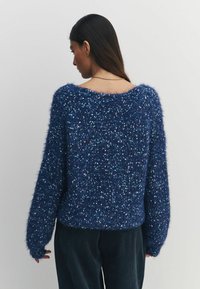 Granatowy, puszysty sweter z dzianiny o luźnym kroju, opadających ramionach i subtelnych wariacjach tekstury. Żebrowane mankiety i detal u dołu.