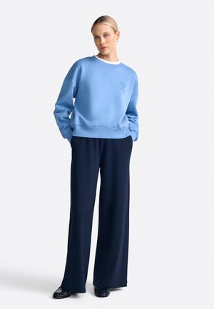 Felpa azzurra chiara con scollatura rotonda e spalle scese, abbinata a pantaloni navy a gamba larga, creando una silhouette rilassata.