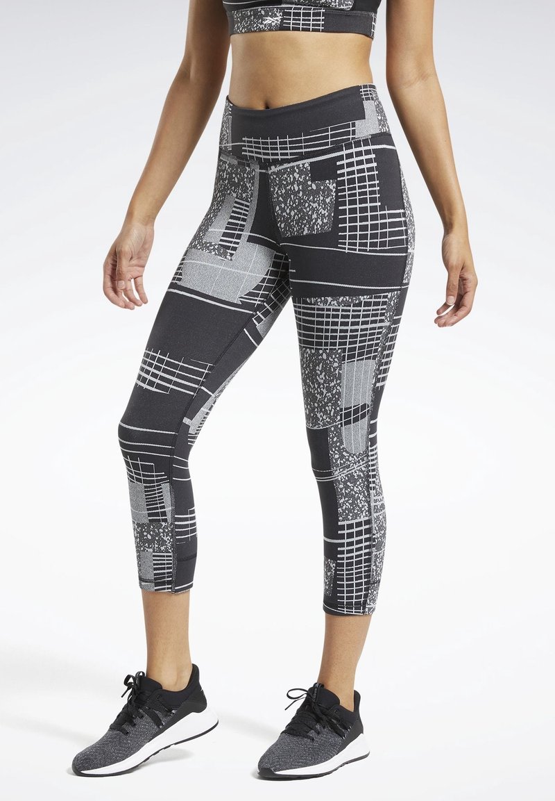 Czarne i szare legginsy capri z geometrycznymi wzorami, z wysokim stanem, elastycznym materiałem i smukłym designem. Połączone z czarnymi butami sportowymi.