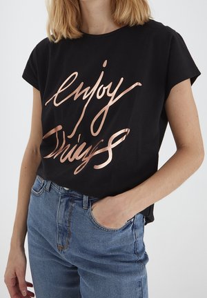 Sort T-shirt med "Enjoy Things" i metallisk roseguld tekst. Korte ærmer, afslappet pasform, parret med lyseblå denim jeans.