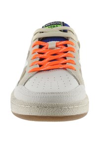 Zapatilla con un upper de cuero crema, cordones naranjas brillantes que contrastan, lengüeta azul y acentos texturizados. Presenta perforaciones en la zona de los dedos.