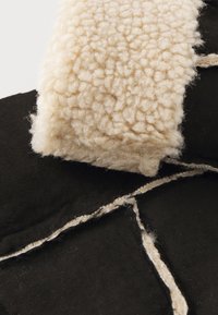 Black fabric with a textured, cream-colored fleece accent. Fleece features small, rounded tufts; fabric has frayed edges and visible stitching details.