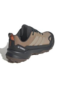 Brązowo-czarny but do wędrówek Adidas Terrex z teksturowaną podeszwą, wyściełanym kołnierzem i czarnymi sznurówkami z niebieskimi akcentami, ustawiony pod kątem, aby pokazać boczną stronę.