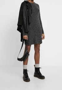 Abito maglia grigio a costine con maniche lunghe, abbinato a una giacca di pelle nera. Stivali neri con lacci e calze grigie di maglia completano il look.