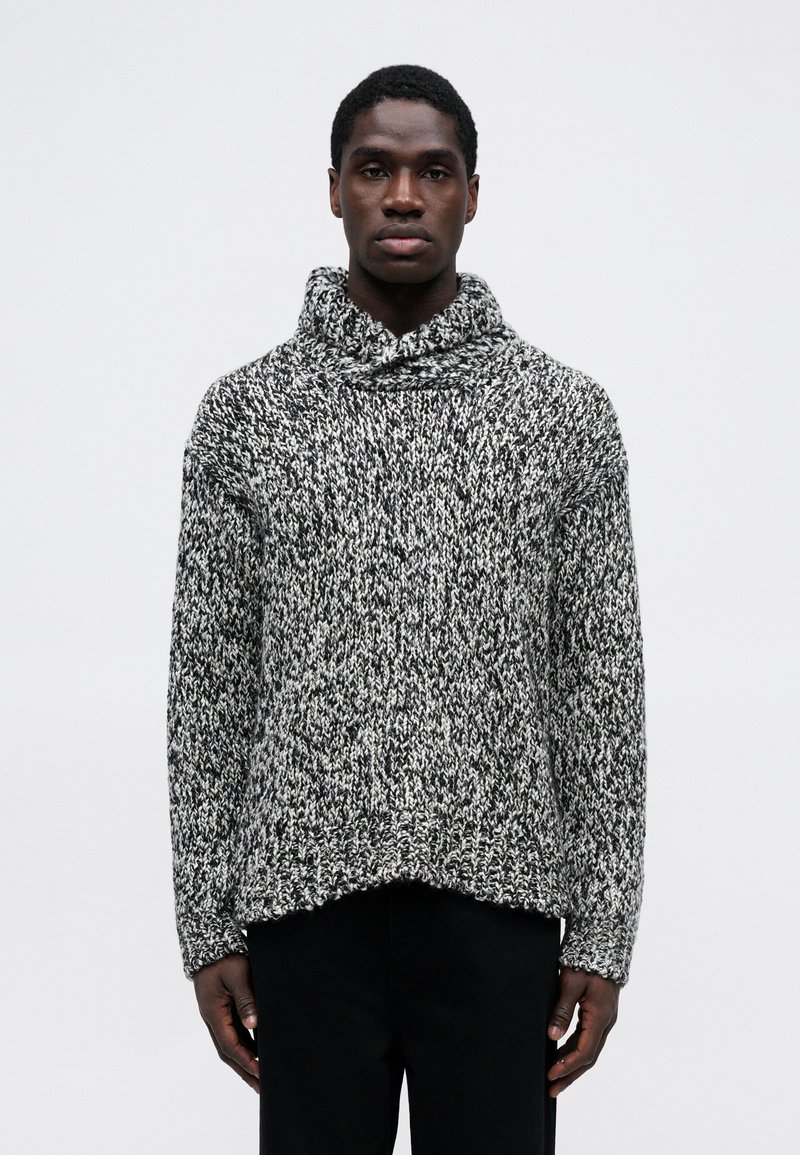 Maglione lavorato a maglia spesso in bianco e nero con un colletto alto e ripiegato. Presenta un motivo testurizzato e una silhouette rilassata e oversize.