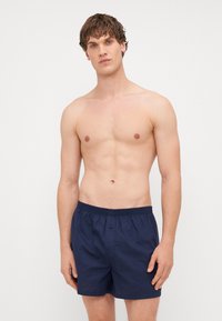 Calções de banho azul-marinho com cintura elástica e fecho com botão, apresentando uma textura suave e um corte casual. Sem padrões ou detalhes visíveis.