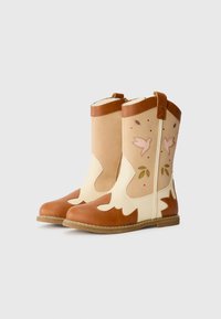 Brown and cream ankle boots with a floral cut-out design, leather material, rounded toe, and a slight heel. Stitched accents on the sides.