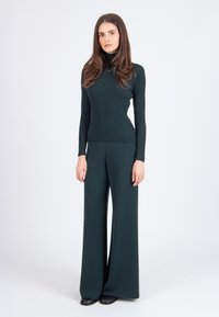 Dark green ribbed turtleneck sweater paired with matching wide-leg trousers, both made of textured knit fabric. Black shoes complete the outfit.