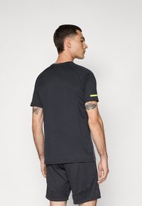 Svart treningstrøye med korte ermer og rund hals, med slim fit og en liten gul detalj på ermet.