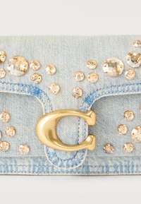 Φωτεινό γαλάζιο τσαντάκι από τζιν με χρυσό κούμπωμα «C» και διάσπαρτους στρογγυλούς διακοσμητικούς λίθους κεχριμπαριού.