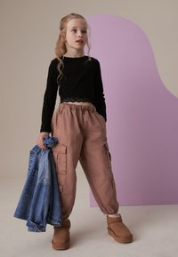 Juodas ilgas rankovėmis viršus su nėriniu, rožinės spalvos krovinių kelnės ir rudos spalvos auliniai bateliai. Džinsinis švarkas per petį. Minkšta tekstūra, kasdieniškas dizainas.