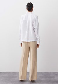 White linen shirt with long sleeves and a back seam, paired with high-waisted beige wide-leg trousers and stiletto heels.