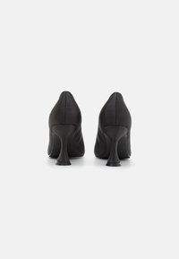 Zapatos de tacón alto negros con parte superior de textil suave y un diseño de tacón acampanado distintivo. Silueta elegante y minimalista.