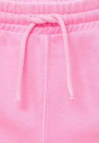 Roza bombažna trenirka s pletenico za zapiranje, ki ima mehak teksturo in elastiko v pasu. Vključuje podrobnosti šivanja ob šivih.