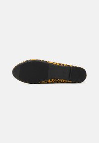 Leopardmønster flate sko med et gult og svart design, med en teksturert gummisåle og en glatt, tekstiloverdel.