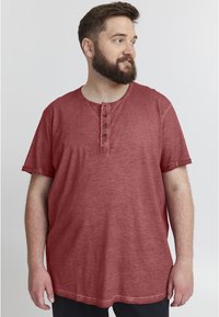 Rød kortærmet henley-skjorte i blødt, struktureret stof med fire knapper og bred rund halsudskæring. Løs pasform, der går til hofterne.