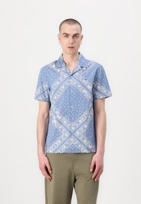 Camicetta azzurro chiaro a maniche corte con motivo paisley bianco e accenti diagonali. Presenta un colletto a camicia e apertura con bottoni.