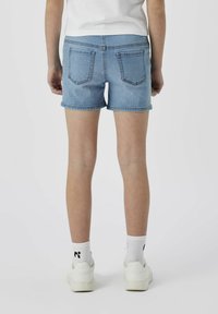 Shorts de denim en azul claro con corte recto, dobladillo vuelto y dos bolsillos traseros. Llevados con zapatillas blancas y calcetines con un logo negro.