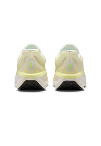 Un paio di scarpe da corsa di colore giallo chiaro e bianco viste da dietro, con suole nere texturizzate e strisce verticali riflettenti sul tallone.