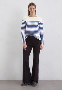 Pasiasty sweter z długim rękawem w białym i niebieskim kolorze, zestawiony z czarnymi spodniami z szerokimi nogawkami. Sweter ma okrągły dekolt i prążkowany dół.