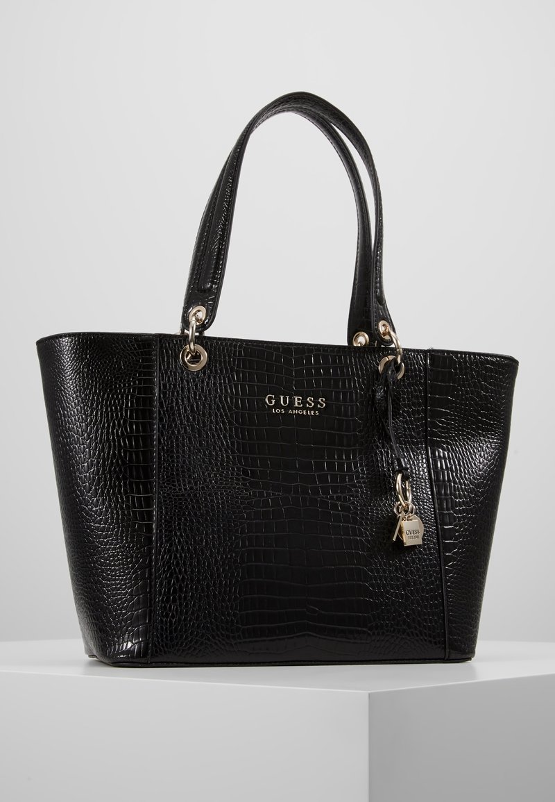 Sac fourre-tout en simili cuir noir avec un motif crocodile texturé, une quincaillerie dorée et un charm logo décoratif. Poignées doubles pour le transport.