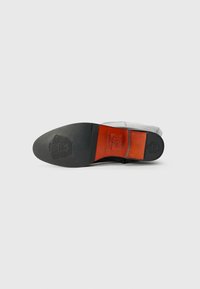 Talpă de pantof din piele neagră cu accente roșii și negre. Prezintă o suprafață texturată, detalii cu logo și o formă conică pentru un stil formal.