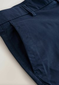 Pantalon bleu marine avec poche latérale, passants pour ceinture et coutures visibles sur une surface claire.