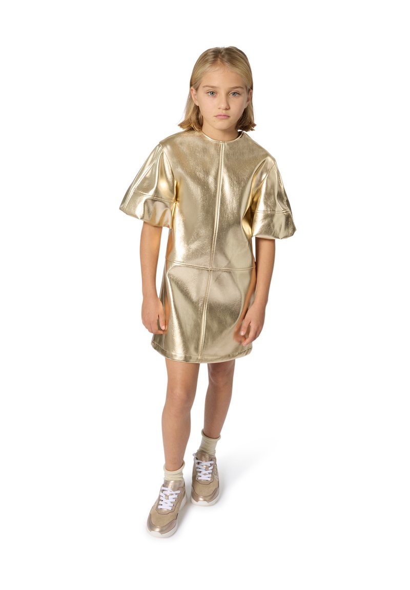 Robe dorée métallisée à manches courtes avec un design d'épaule sans couture, dotée d'un col rond et de manches évasées, associée à des baskets beiges.