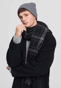 Szary dzianinowy beret, czarona szal w kratę i czarna kurtka noszone na szarym swetrze. Materiały wydają się miękkie, z prostym wzornictwem i teksturowanym dzianinowym splotem.