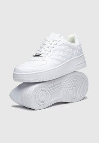 Sneakers bianchi con parte superiore testurizzata, caratterizzati da un motivo a logo ripetuto, lacci rotondi e una suola spessa con un design a battistrada circolare.