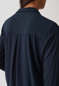 Marineblauwe shirt met een soepele textuur, voorzien van een contrasterend donkerder paneel op de bovenrug en een klassiek kraagontwerp.
