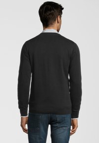 Svart tröja med långa ärmar, ribbade mudd och nederkant, bärs över en vit skjorta. Mjuk struktur, enkel design och figurnära passform.