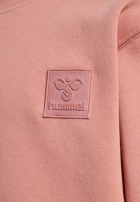 Persikofärgad sweatshirt med en texturerad, rektangulär gummilogg med "hummel"-text och emblem. Mjuk, stickad bomull.