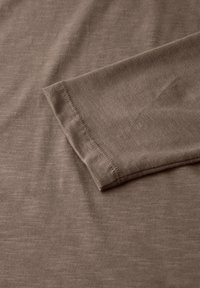 Brauner Baumwollstoff mit glatter Textur, mit einem genähten Saum und einer lässigen Passform. Nahaufnahme des Ärmeldetails.