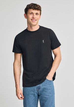 Zwarte katoenen t-shirt met een ronde hals en korte mouwen. Bevat een klein logo op de borst en heeft een ontspannen pasvorm. Gekocht met lichtblauwe jeans.