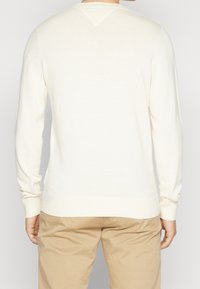 Maglione a maniche lunghe color crema con polsini e orlo a coste, caratterizzato da un dettaglio a forma di V nel retro del collo e una texture liscia.
