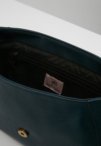 Tearfärgad konstläderhandväska med en slät yta, som har ett guld snap-stängning och en zippered innerficka. Etiketten säger "ANNA FIELD."