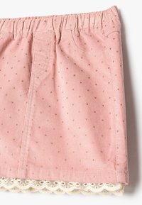 Falda de pana rosa con un patrón de estrellas doradas y un dobladillo de encaje. Presenta una cinturilla elástica y dos pequeños bolsillos frontales.