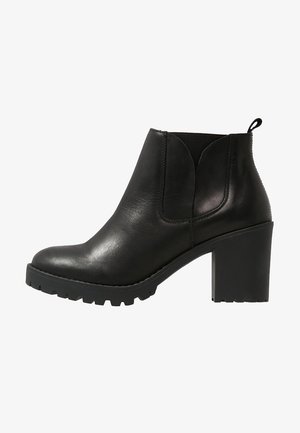 Bottine en cuir noir avec un bout arrondi, un talon bloc, des panneaux latéraux élastiques et une semelle en caoutchouc à relief. Texture lisse avec un léger éclat.