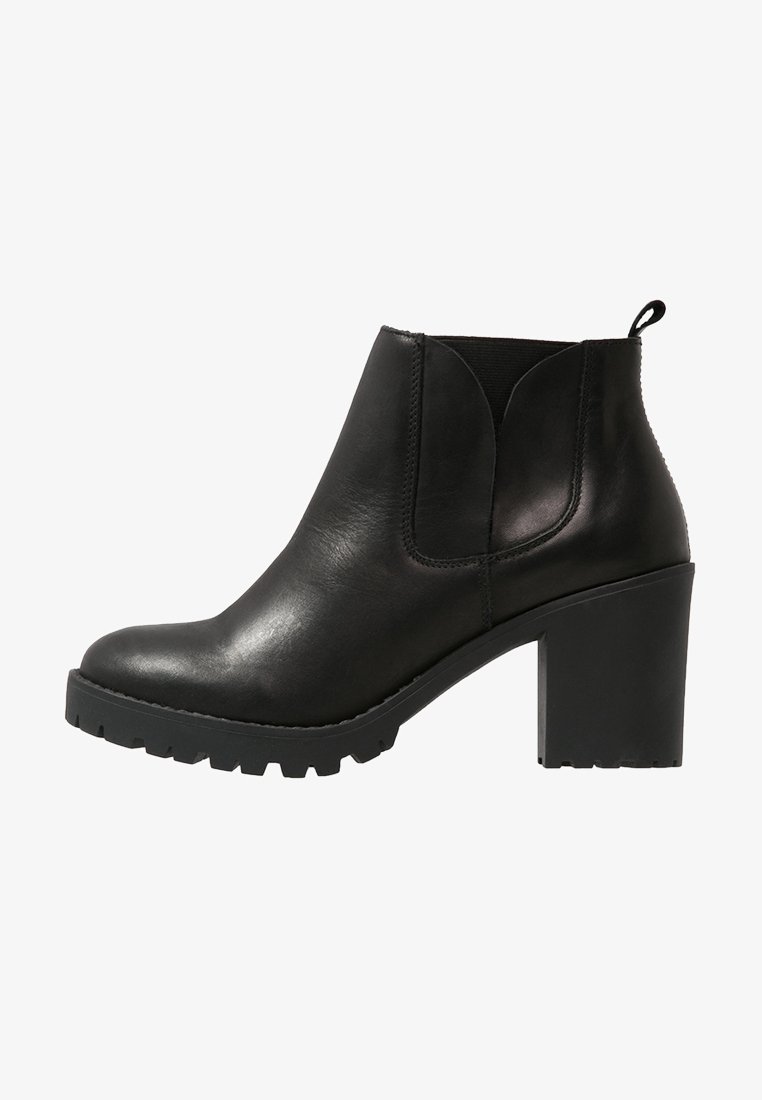 Bottine en cuir noir avec un bout arrondi, un talon bloc, des panneaux latéraux élastiques et une semelle en caoutchouc à relief. Texture lisse avec un léger éclat.