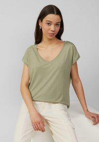 Jasnozielona, krótko rękawowa koszulka typu V z miękkiego materiału, zestawiona z kremowymi spodniami. Charakteryzuje się luźnym krojem i minimalistycznym designem.