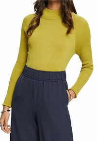 Haut à manches longues côtelé en jaune-vert vif, avec un col montant. Associé à un pantalon bleu marine à taille élastique. Bracelet argenté au poignet.