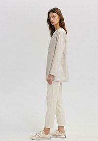 Beige langærmet top med en afslappet pasform, parret med off-white tapered bukser og beige sneakers. Let stof, minimalistisk design.