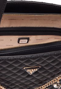 Borsa a tracolla nera trapuntata con hardware dorato, caratterizzata da un interno con marchio e scomparti con cerniera. Gli accenti includono un dettaglio a catena.
