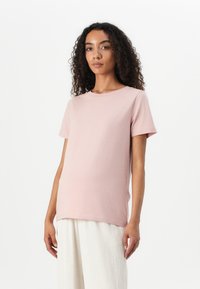 Light pink short-sleeve t-shirt made of soft cotton material, featuring a round neckline and a relaxed fit, paired with light-colored trousers.