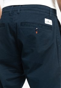 Pantalons bleu marine en coton, dotés d'une poche arrière avec fermeture à bouton, d'un accent en fil orange et d'une étiquette de logo.